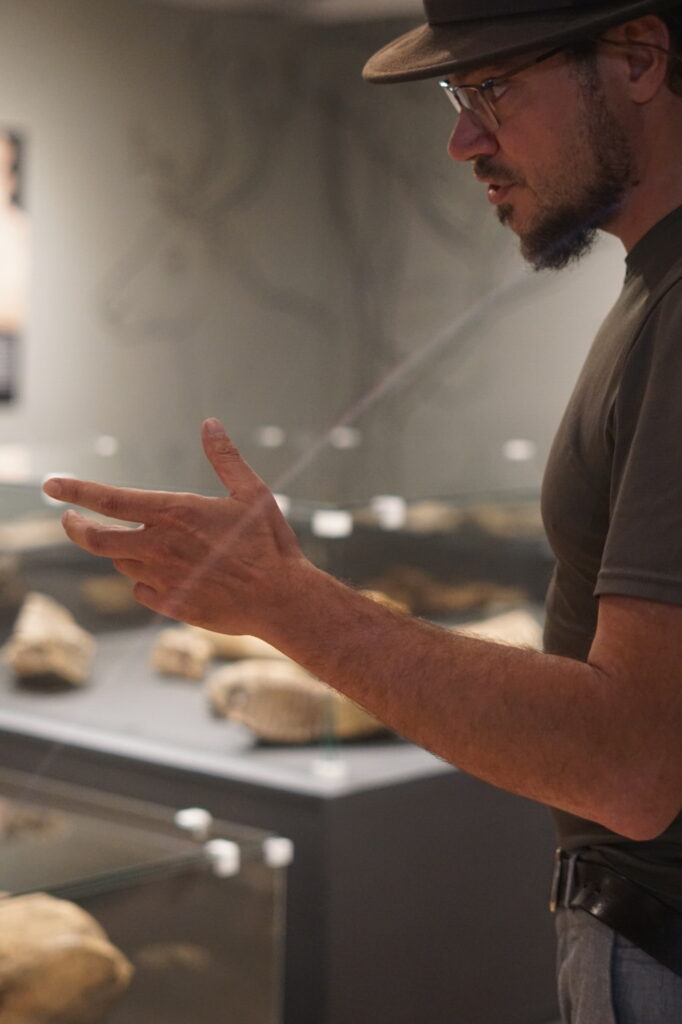 Adam Wawrusiewicz z Działu Archeologii Muzeum Podlaskiego w Białymstoku opowiadający o zbiorach historii naturalnej z wystawy “W kamień zmienione. 70 lat Działu Archeologii” towarzyszącej ekspozycji „Skarby minionych wieków. 70 lat Działu Archeologii”.© A. Cetwińska, na licencji CC BY SA 4.0